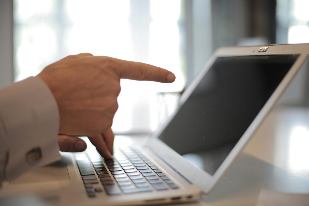 Businessman's hand pointing at laptop screen indoors, emphasizing technology use.